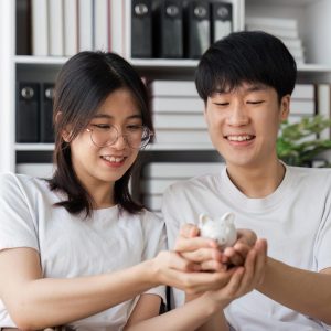 Smiling, happy young family together put coins in piggy bank to save money. Married couple are planning to save up finances. Savings, investments, financial freedom, business, hope for success.