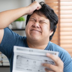 Asian sad and worried man going crazy with bill payment amount. Businessman worried with monthly bills to paid. Negative facial expressoion with paper overdue bill.