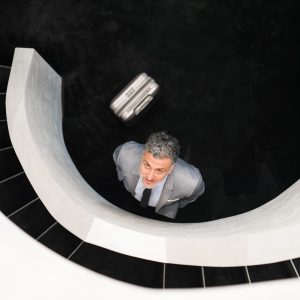 Businessman with suitcase standing at the bottom of the staircase, looking up. Top view.