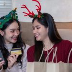 Lesbian couple enjoys a cheerful holiday shopping session, utilizing technology to share joyous festive moments together.
