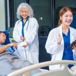 Two female doctors examine a patient lying on a hospital bed,discuss the medical chart,administer