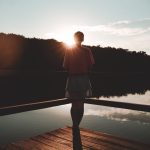 Young woman stands on a wooden bridge near lake on green nature background. Travel, Freedom, Lifestyle concept. Female enjoy outdoors. Slovenia, Europe. Domestic tourism