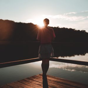 Young woman stands on a wooden bridge near lake on green nature background. Travel, Freedom, Lifestyle concept. Female enjoy outdoors. Slovenia, Europe. Domestic tourism