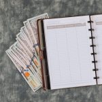 Workplace with notepad with one hundred dollar bills on flat view