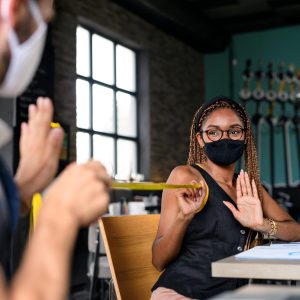 Portrait of young businesspeople with face masks working indoors in office, keeping safe distance.